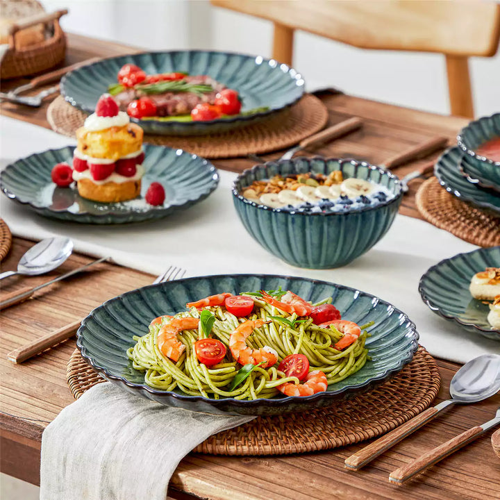 Adonis green reactive glaze stoneware 16 piece dinnerware set close up with food on brown wood table and white runner.