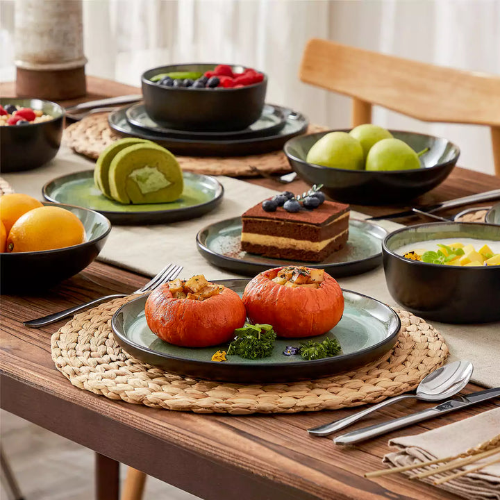 Amber green reactive glaze stoneware 16 piece dinnerware set with roasted pumpkin dessert and fruit on wooden table.