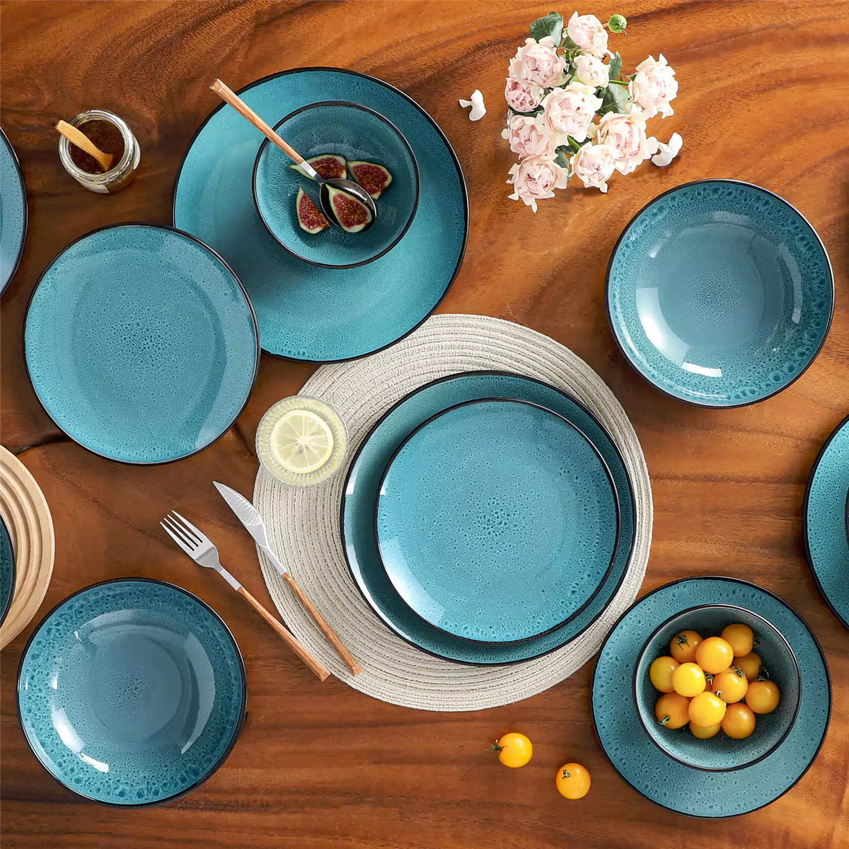 Modern farmhouse dinnerware set with glossy reactive glaze, green plates and bowls on wooden table styled with flowers, cherry tomatoes and figs