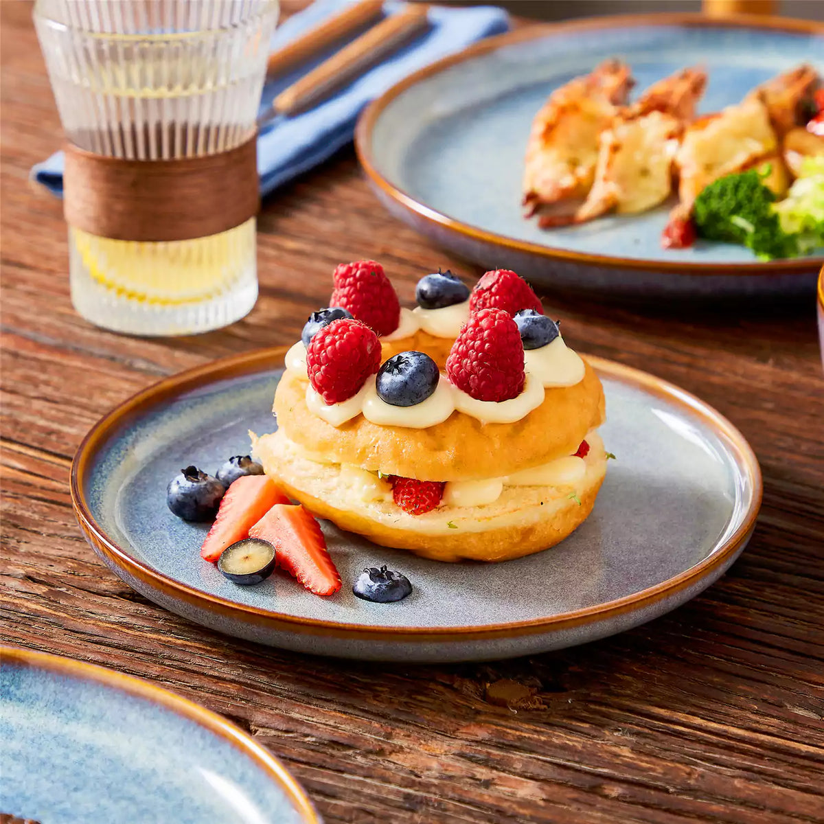 Deep indigo dessert plate with soufflé cake on a wooden table, Playa dinnerware set with cheesy baked shrimp.