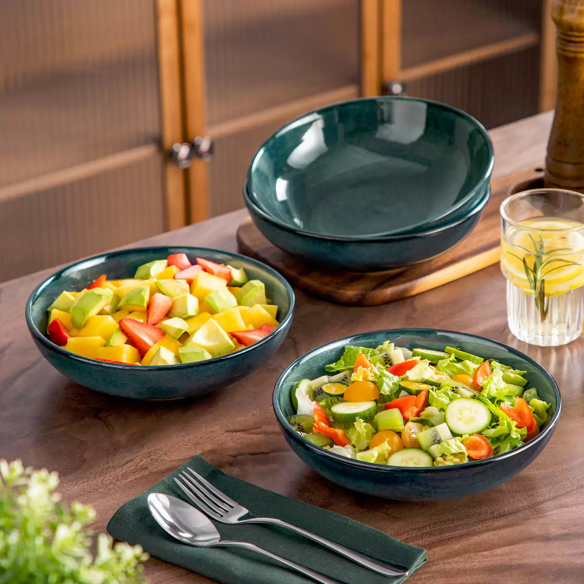 Green stoneware pasta bowl set with salad and greenery on wooden dining table.