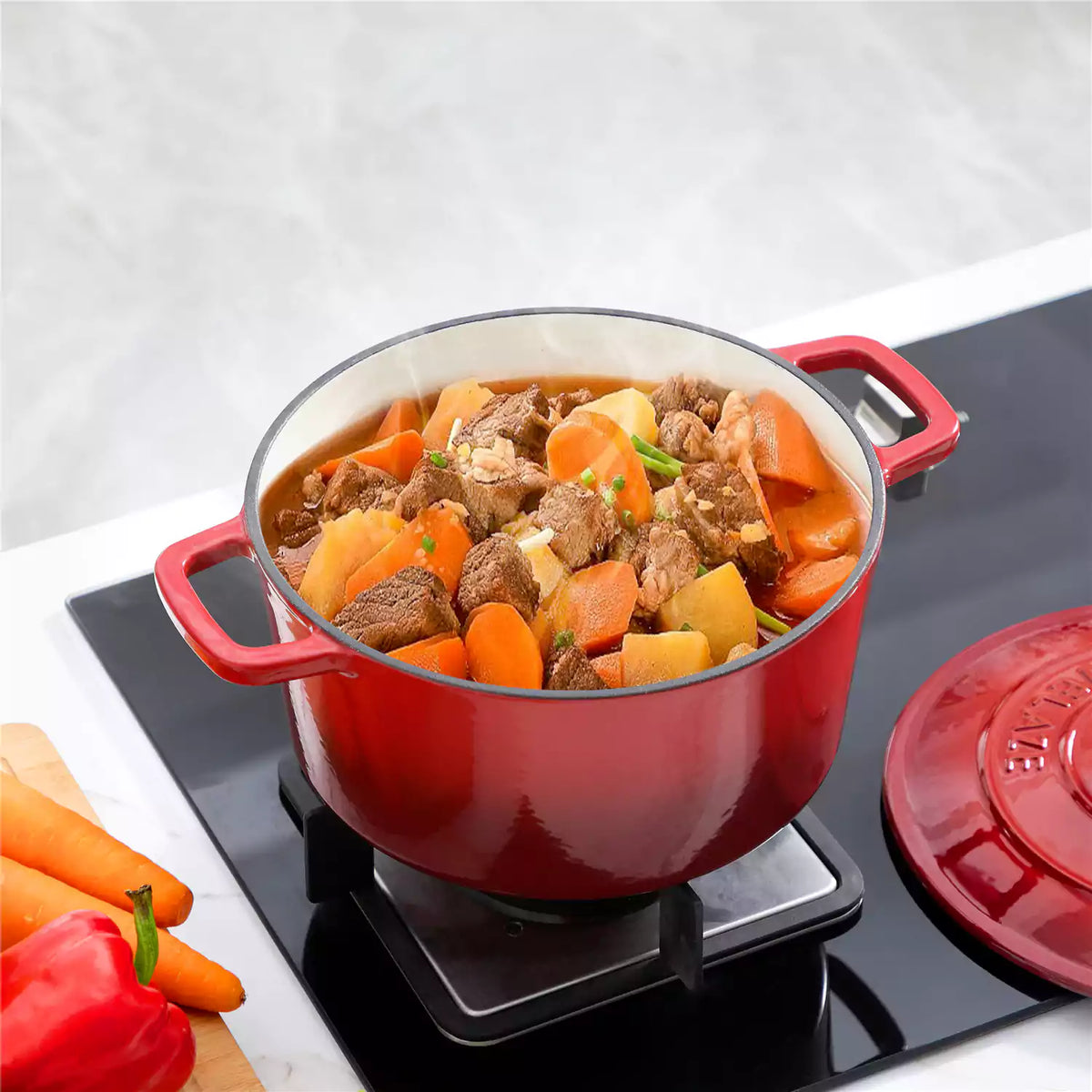 Red 6qt enameled cast iron dutch oven with braised lamb, carrots and potatoes on gas stove.