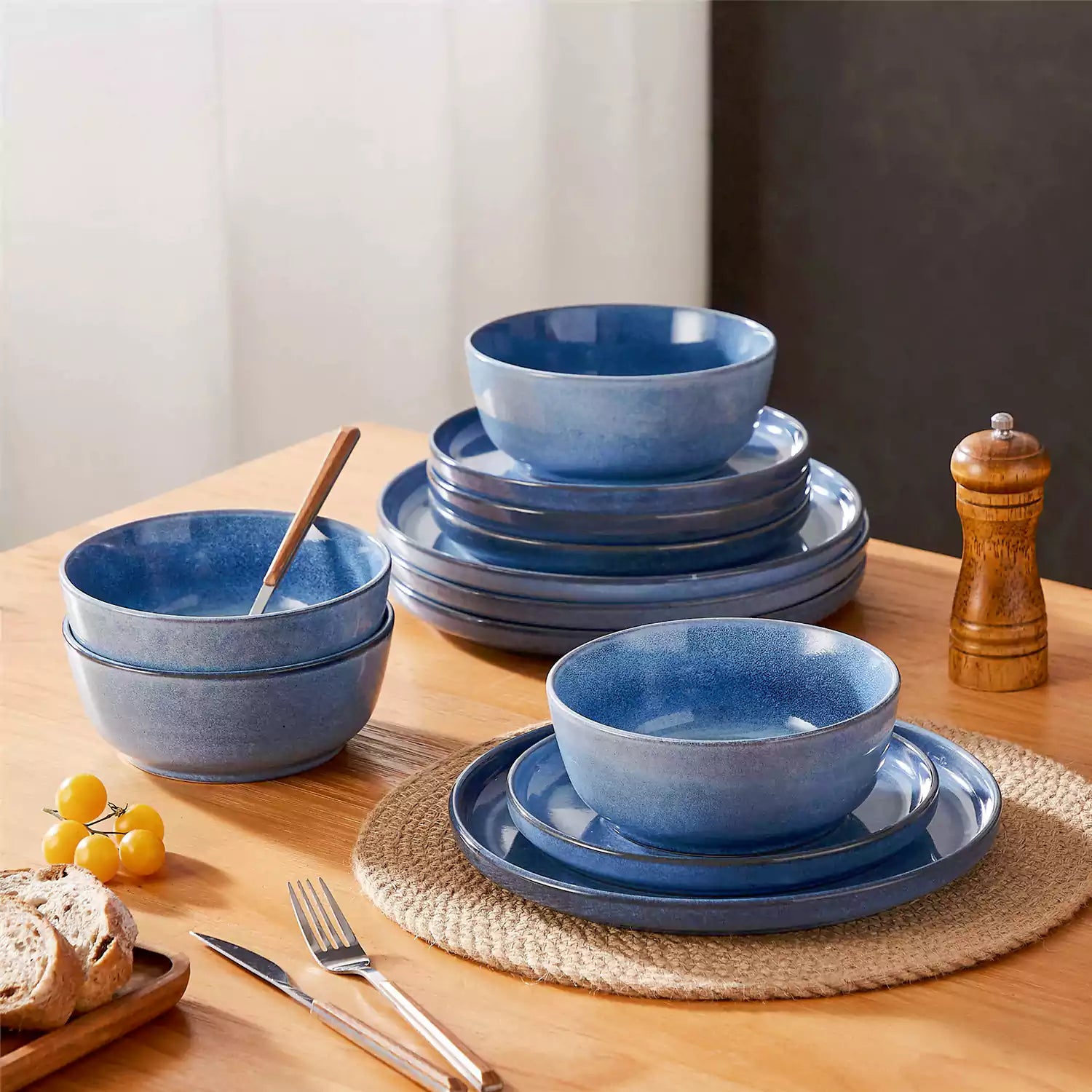 Blue stoneware plates and bowls with reactive glaze on farmhouse wooden table with woven placemats.