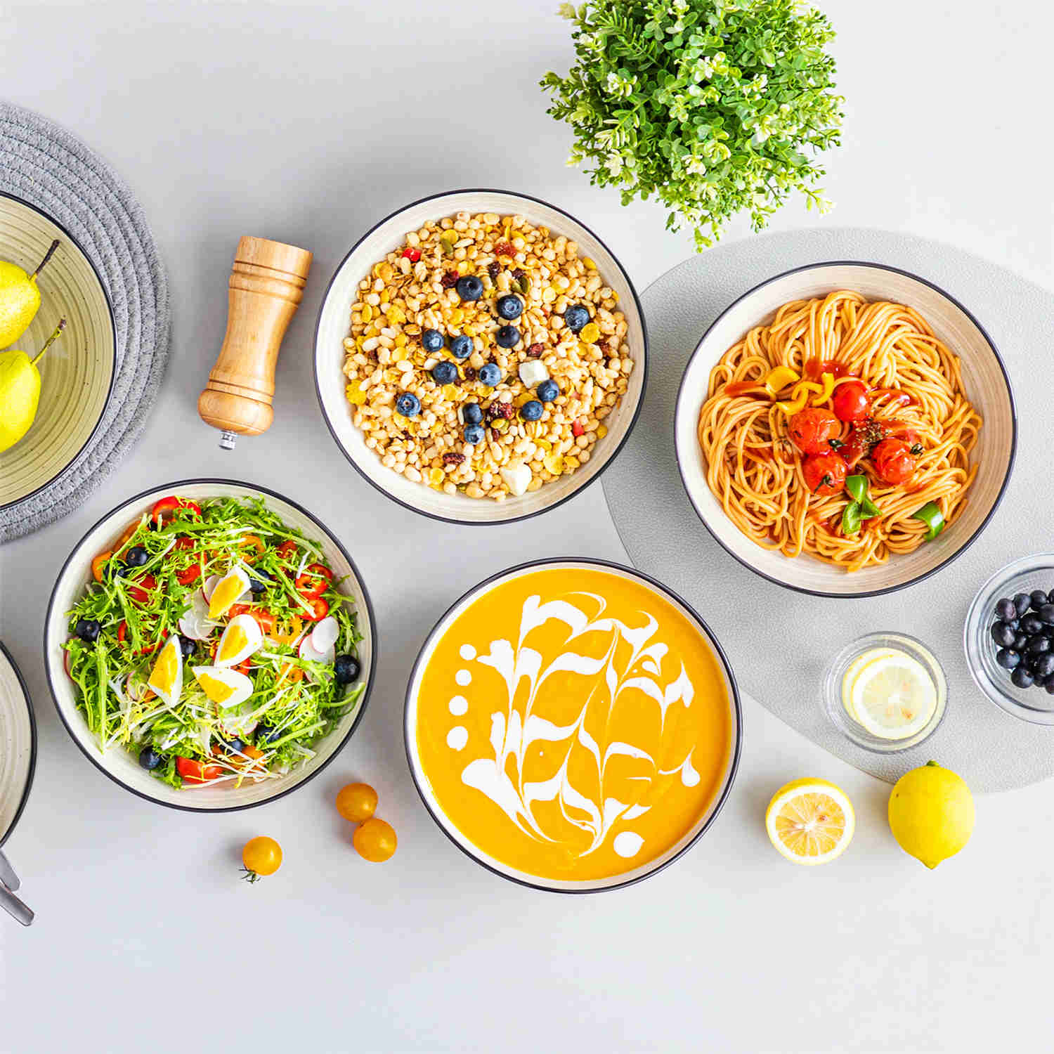 Bonbon double-sided stoneware pasta bowls in beige - artfully filled with pasta - fresh fruit salad - pumpkin soup - and oatmeal - exuding rustic charm on a white dining table