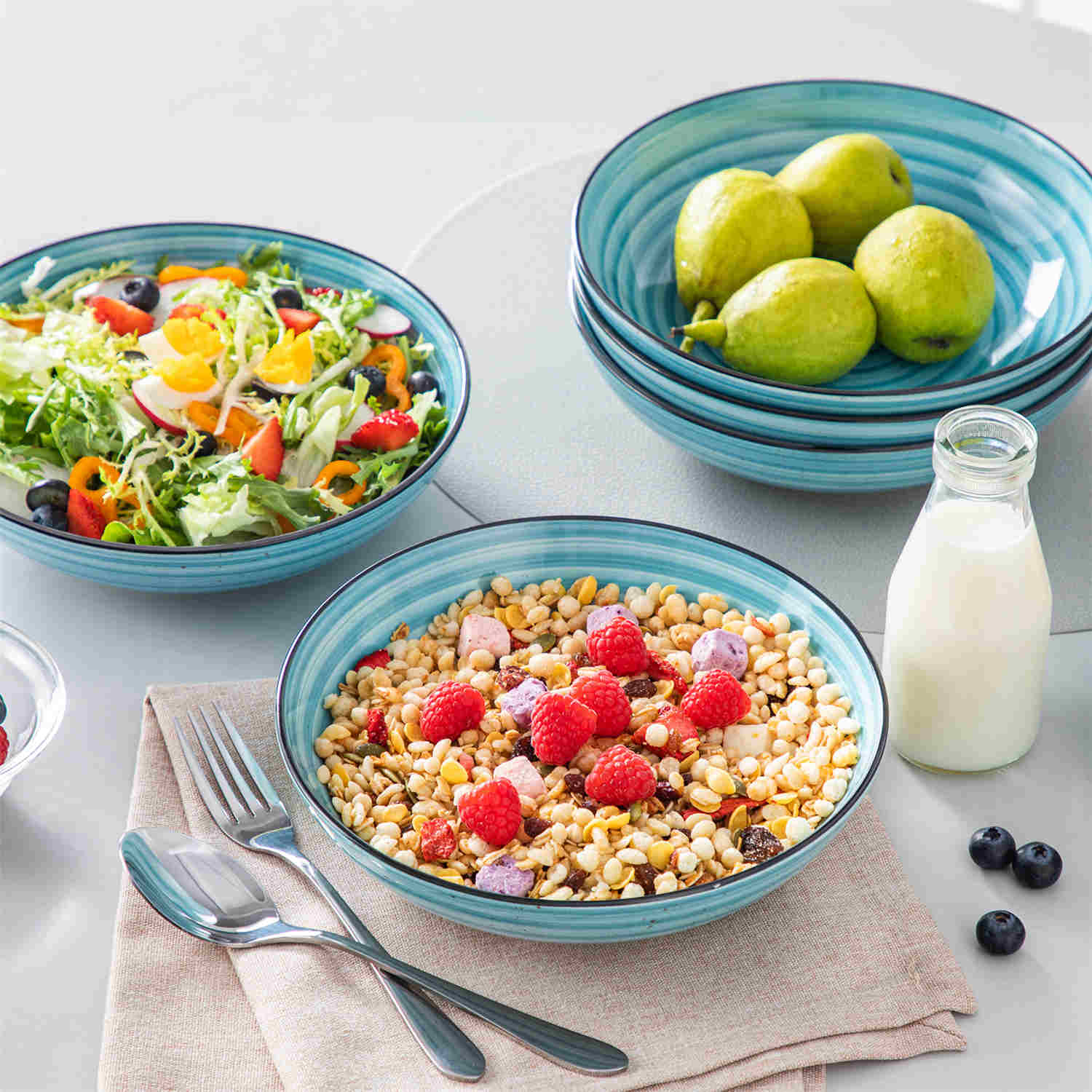 Bonbon double-sided stoneware pasta bowls in blue - artfully filled with pasta - fresh fruit salad - pumpkin soup - and oatmeal - exuding rustic charm on a white dining table