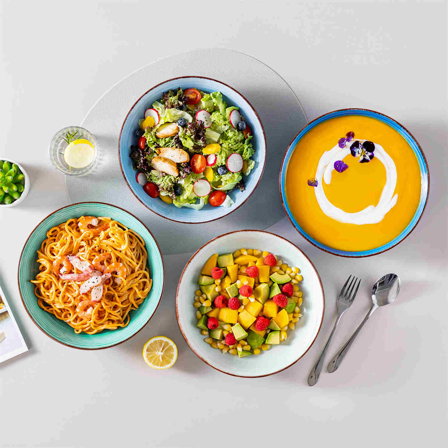 Blue Bonita large stoneware bowls set of 6 on a white table - each filled with pasta - pumpkin soup - and fruit salad - creating a bright and inviting table setting