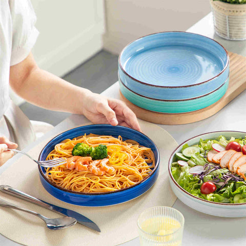 Bonita straight-edge pasta bowls set of 4 on a white table - filled with spaghetti - fruit salad - and mango - accompanied by a small honey jar - ibrant stoneware in ocean blues