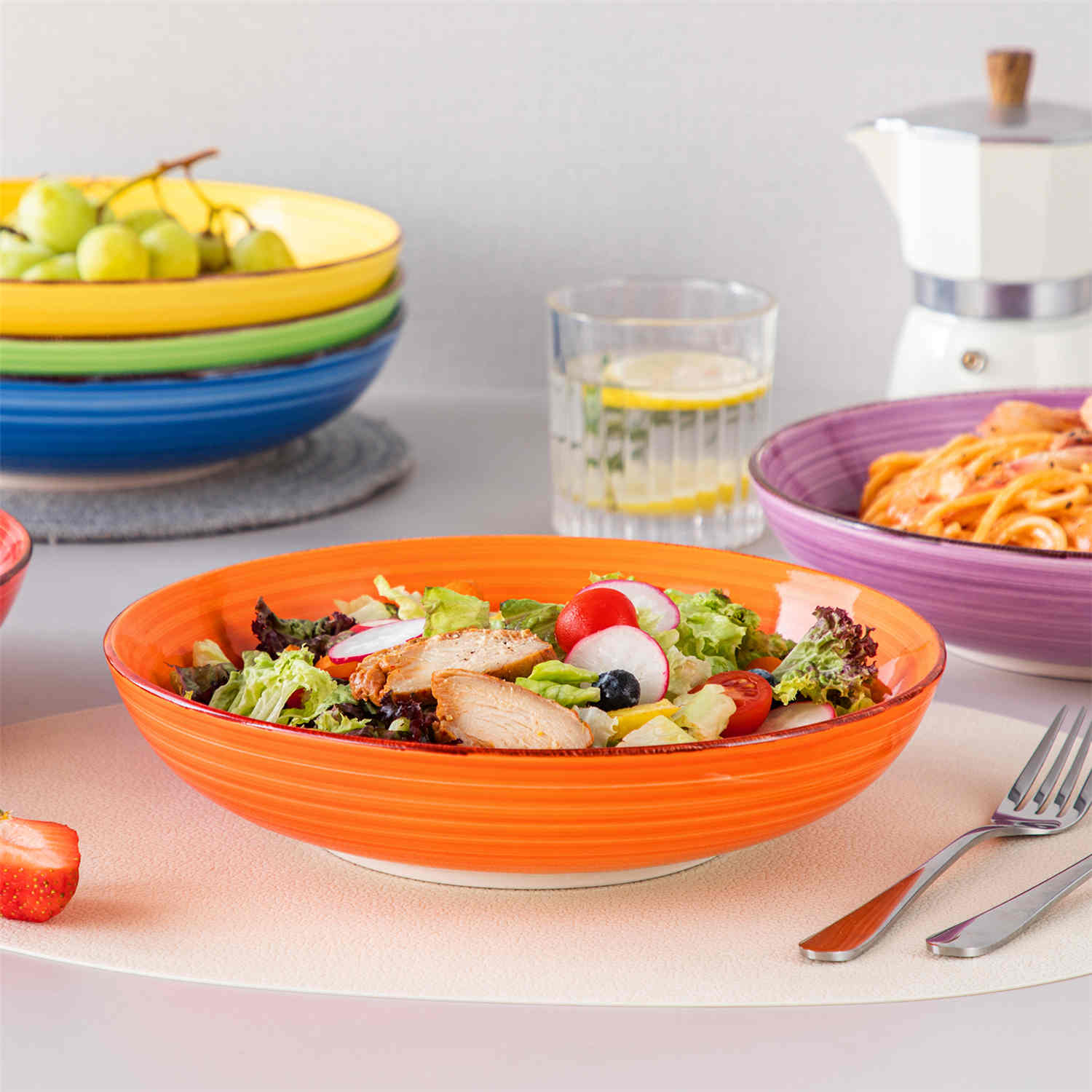 Multicolor Bonita large stoneware bowls set of 6 on a white table - each filled with pasta - pumpkin soup - and fruit salad - creating a bright and inviting table setting