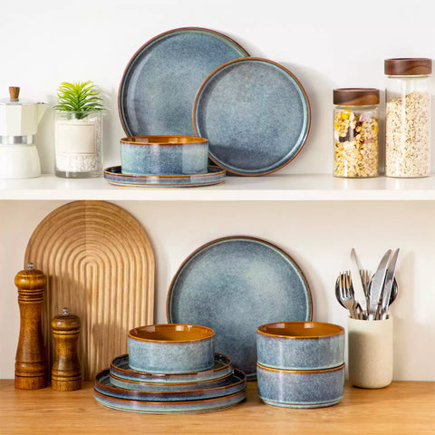 A rustic breakfast spread featuring a plate of meat with vegetables - waffles topped with fruit - and assorted pastries on a white table - complemented by blue stoneware dinnerware