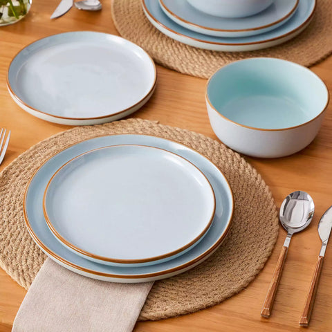 Blue rustic stoneware dinnerware set with speckled - lipped-edge plates and bowls on a dining table with flowers and cutlery in a cozy modern kitchen-vancasso