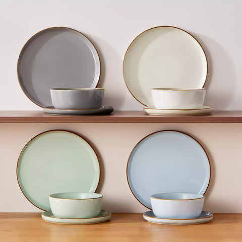 Assorted rustic stoneware dinnerware set with speckled - lipped-edge plates and bowls on a dining table with flowers and cutlery in a cozy modern kitchen-vancasso