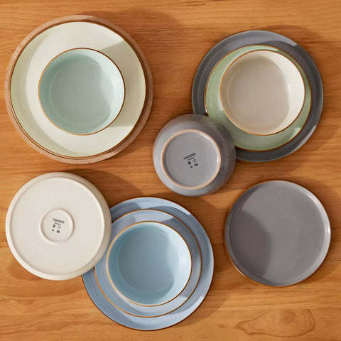 Assorted rustic stoneware dinnerware set with speckled - lipped-edge plates and bowls on a dining table with flowers and cutlery in a cozy modern kitchen-vancasso