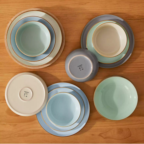 Rustic assorted speckled stoneware dinnerware set with lipped-edge plates and bowls arranged on a sunlit modern dining table-vancasso