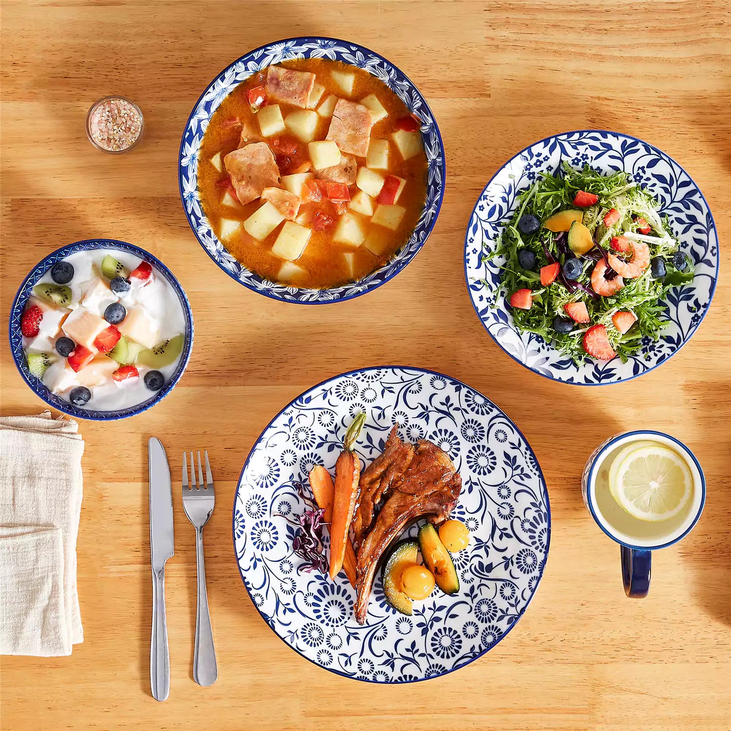 Selene 16-piece porcelain set in indigo patterns - showcasing plates - bowls - and mugs beautifully styled with vibrant meals on a rustic wooden table