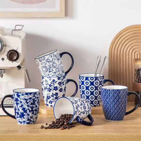 Set of six Japanese-style stoneware mugs in blue and white with indigo patterns, displayed on a kitchen counter with scattered coffee beans