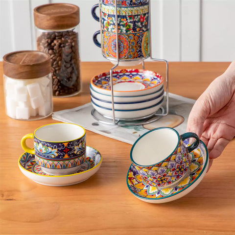 Simi 12 piece porcelain cafe set with 5oz flat white cups and saucers in vibrant boho chic floral patterns on a black metal storage rack with a magazine and napkin on a wooden table