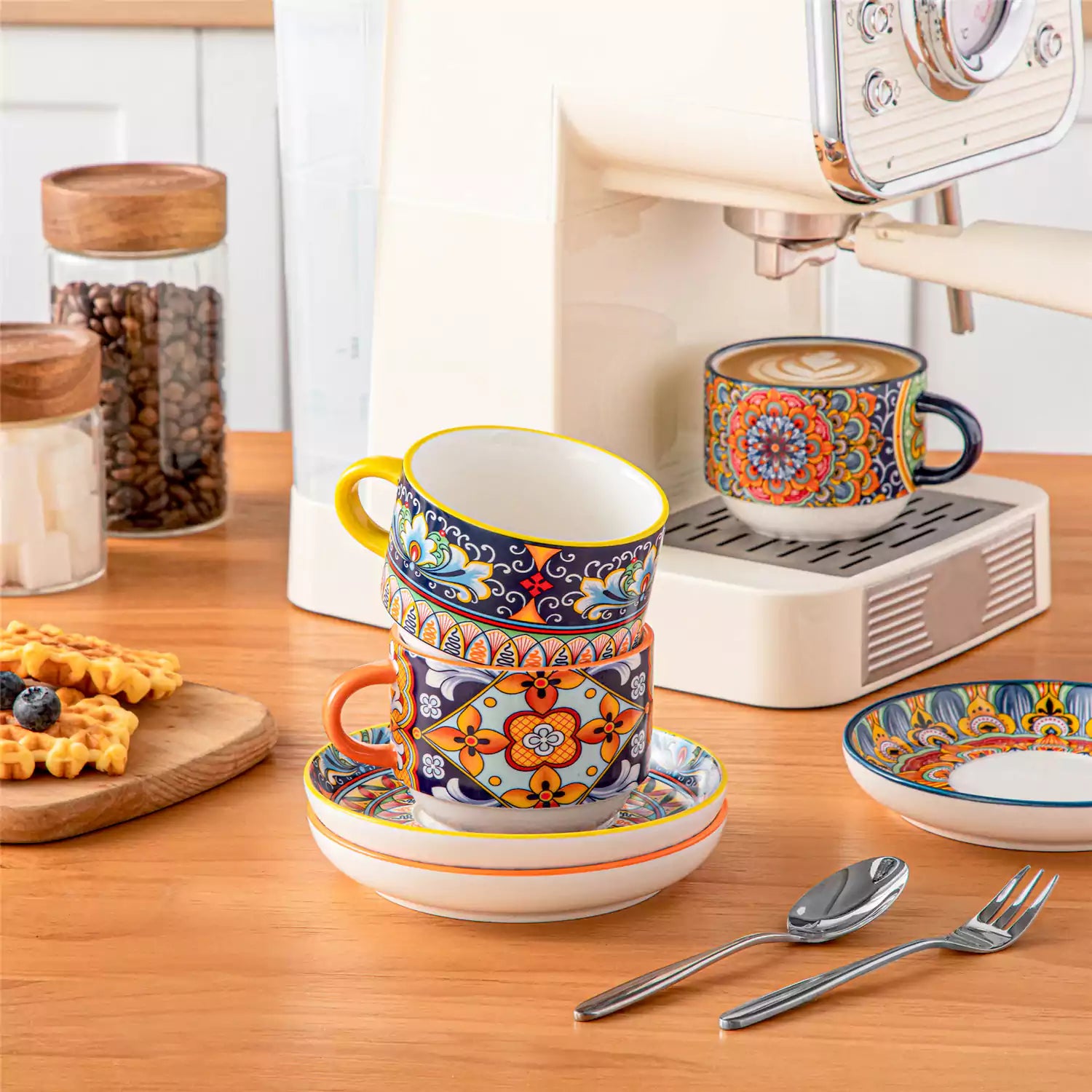 Simi 12 piece porcelain cafe set with 9oz flat white cups and saucers in vibrant boho chic floral patterns on a black metal storage rack with a magazine and napkin on a wooden table