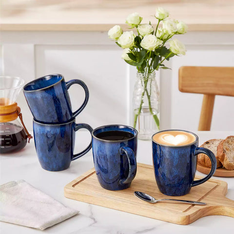 Set of 4 Starry 16oz stoneware mugs in blue with reactive glaze finish styled on a marble countertop with fresh coffee