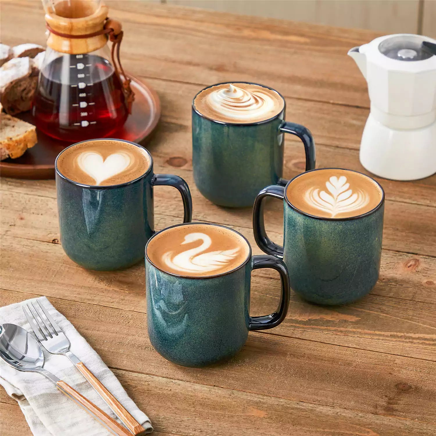 Four starry green 16oz stoneware mugs with latte art on wooden table beside coffee brewing equipment