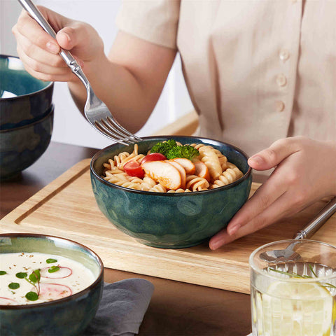 Starry reactive glaze cereal bowls in teal green on a rustic wooden table - filled with creamy soup - pasta - and fresh fruit salad for a cozy - celestial dining vibe
