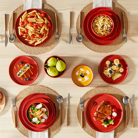 Red reactive glaze stoneware dinner plates styled with food on rustic wood table with woven placemats modern minimalist tableware set