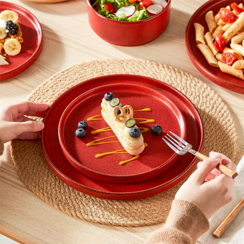 Red reactive glaze stoneware dinner plates styled with food on rustic wood table with woven placemats modern minimalist tableware set