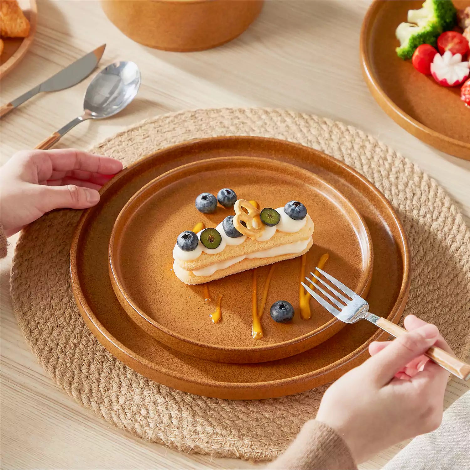 Caramel reactive glaze stoneware dinner plates styled with food on rustic wood table with woven placemats modern minimalist tableware set