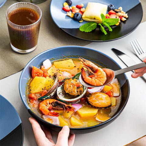 Accel 16-piece blue and black two-tone semi-matte dinnerware set with a large bowl serving seafood soup